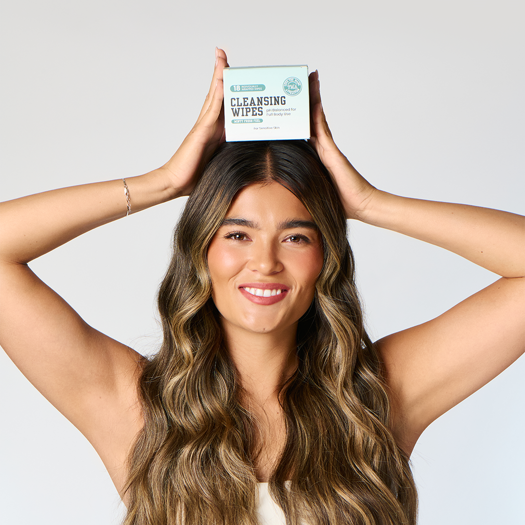 Smiling woman balancing a box of Minty Fresh Cleansing Wipes on her head, showcasing feminine hygiene wipes.